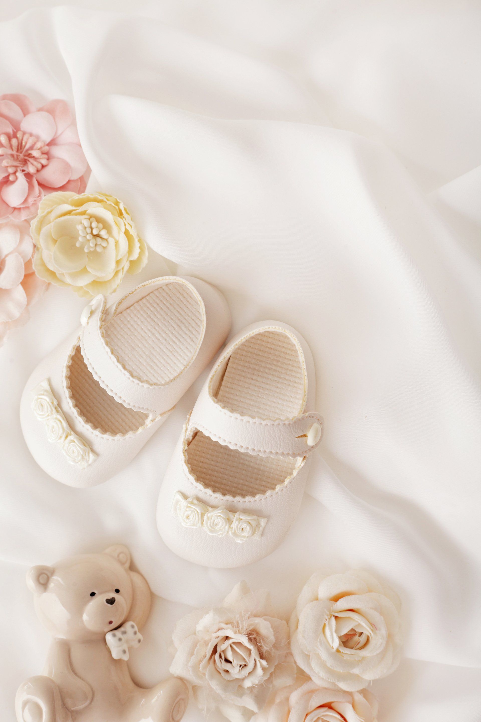 A pair of baby shoes and a teddy bear on a white cloth.