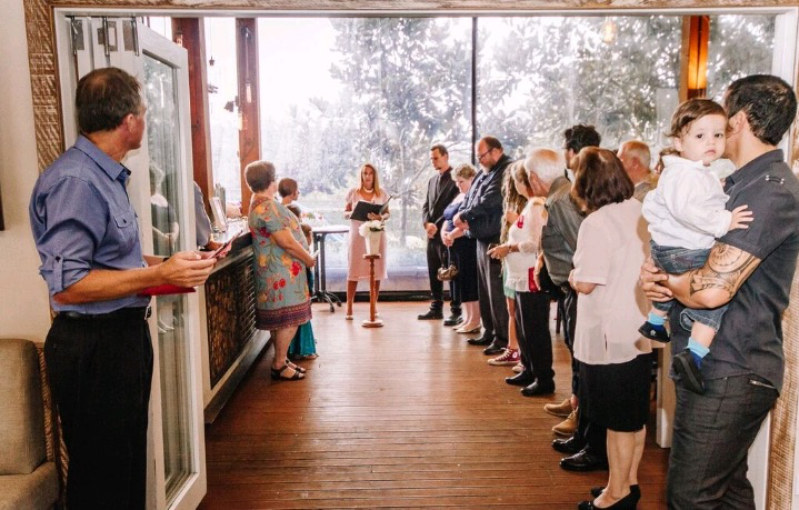 A group of people are standing in a room in front of a window.