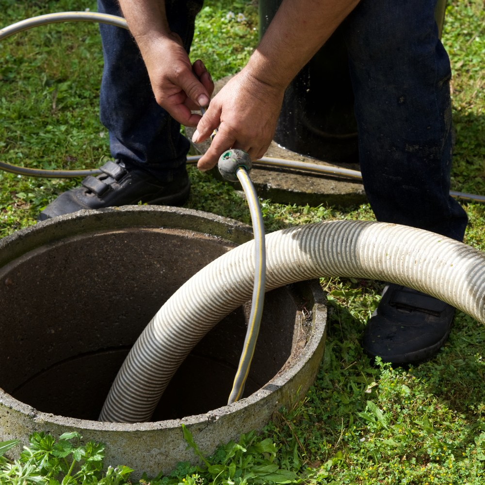 A man is using a vacuum hose to clean a septic tank
