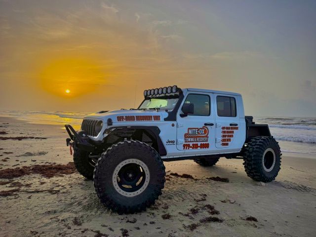 White off-road Jeep Gladiator on a beach at sunset.