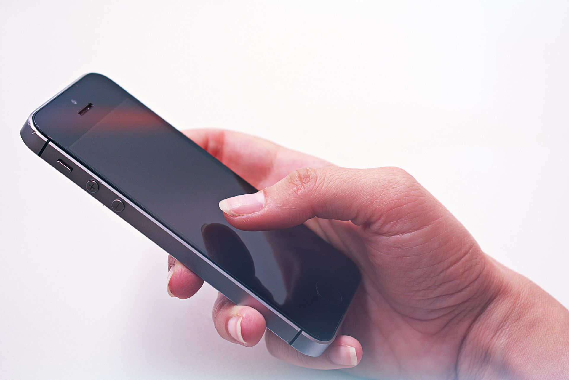 A hand holding a dark-colored smartphone against a plain white background.