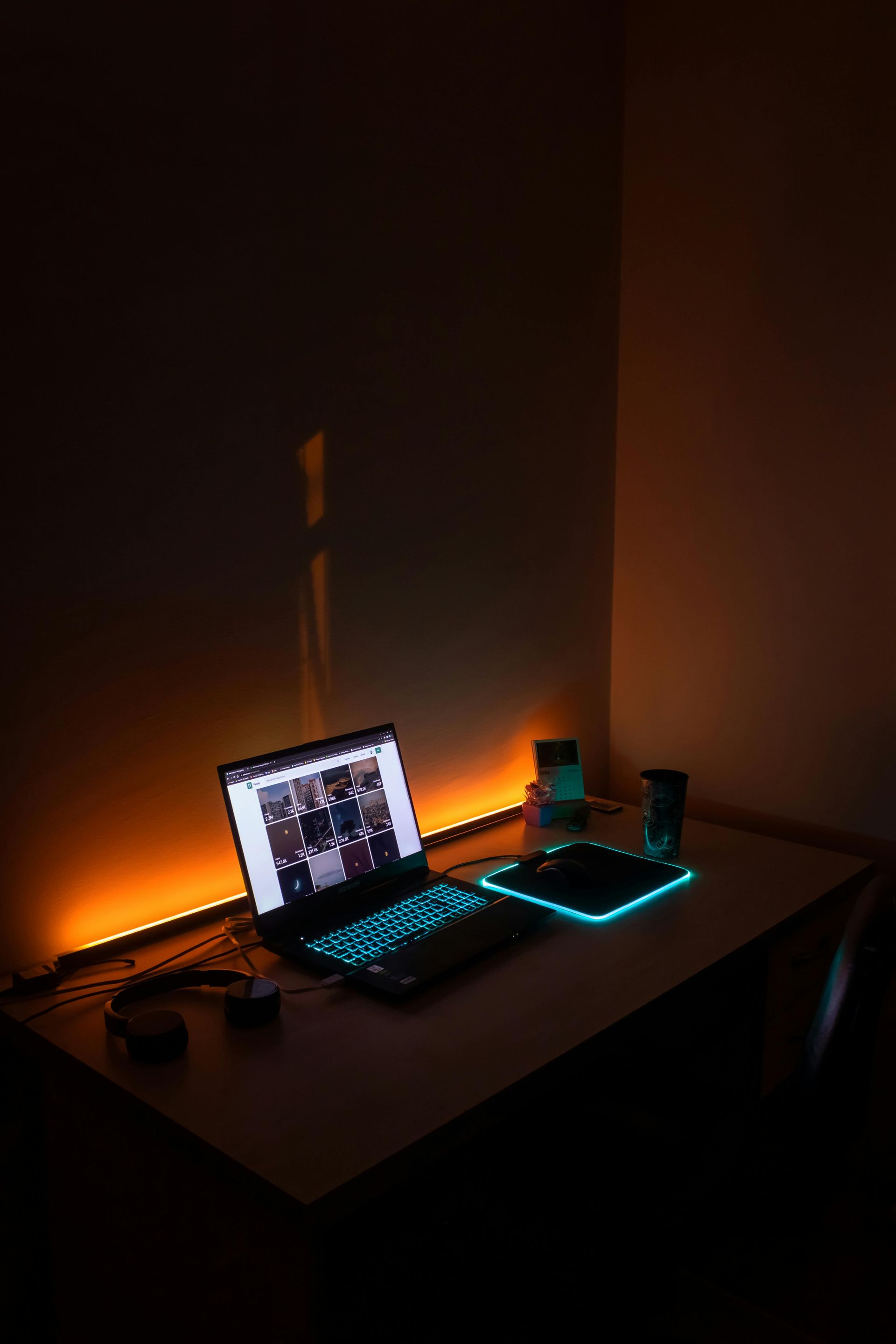 A dimly lit room with an orange-lit desk, featuring a laptop and mousepad glowing with cyan accents.