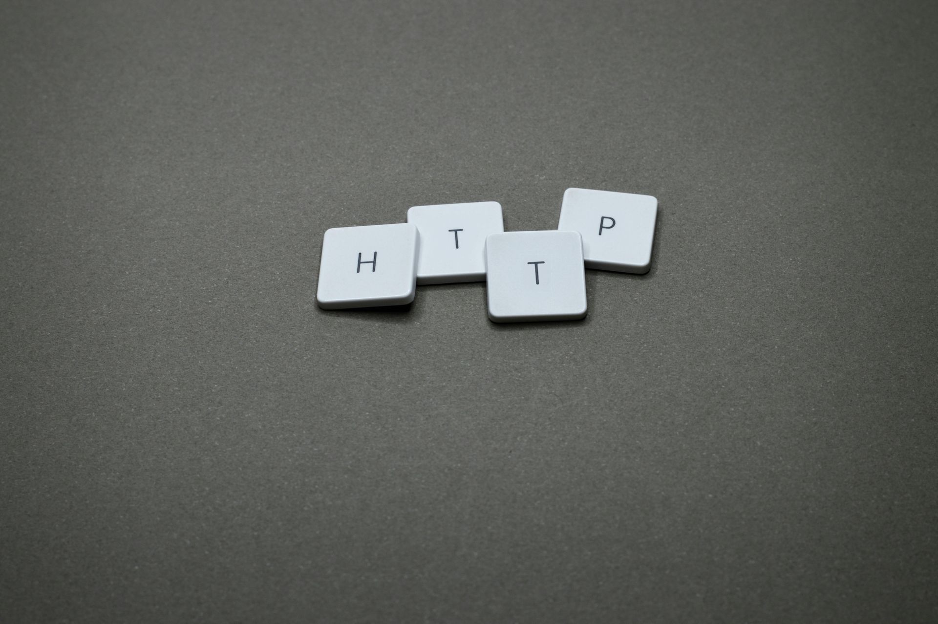Four white keyboard keys labeled H, T, T, and P are scattered on a plain gray background.