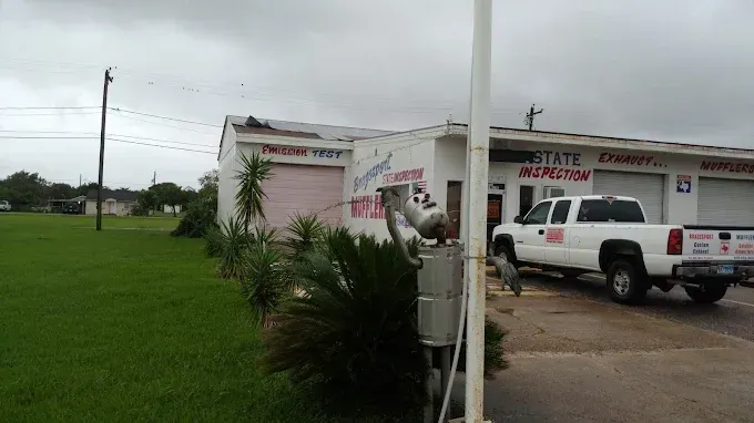 Brazosport Muffler Shop on a cloudy day. White truck parked in front. Green grass and a power pole in the distance.