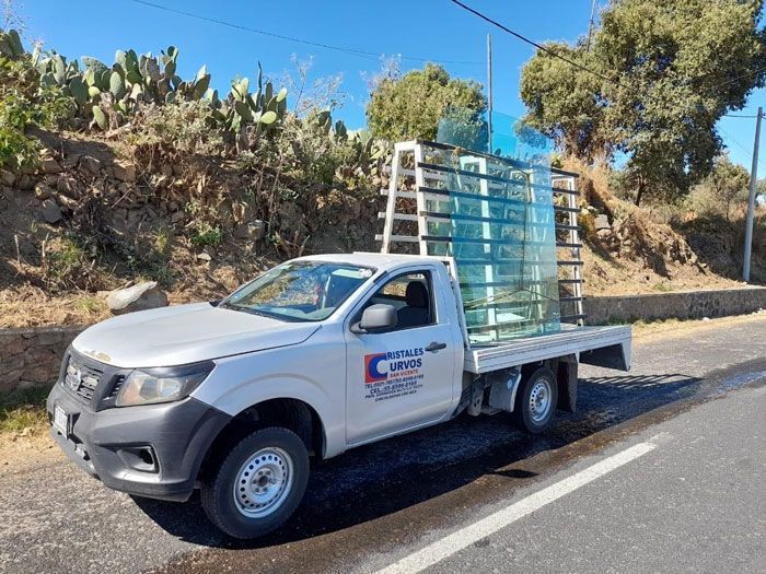 Un camión blanco con una carga de vidrio en la parte trasera está estacionado al costado de la carretera.