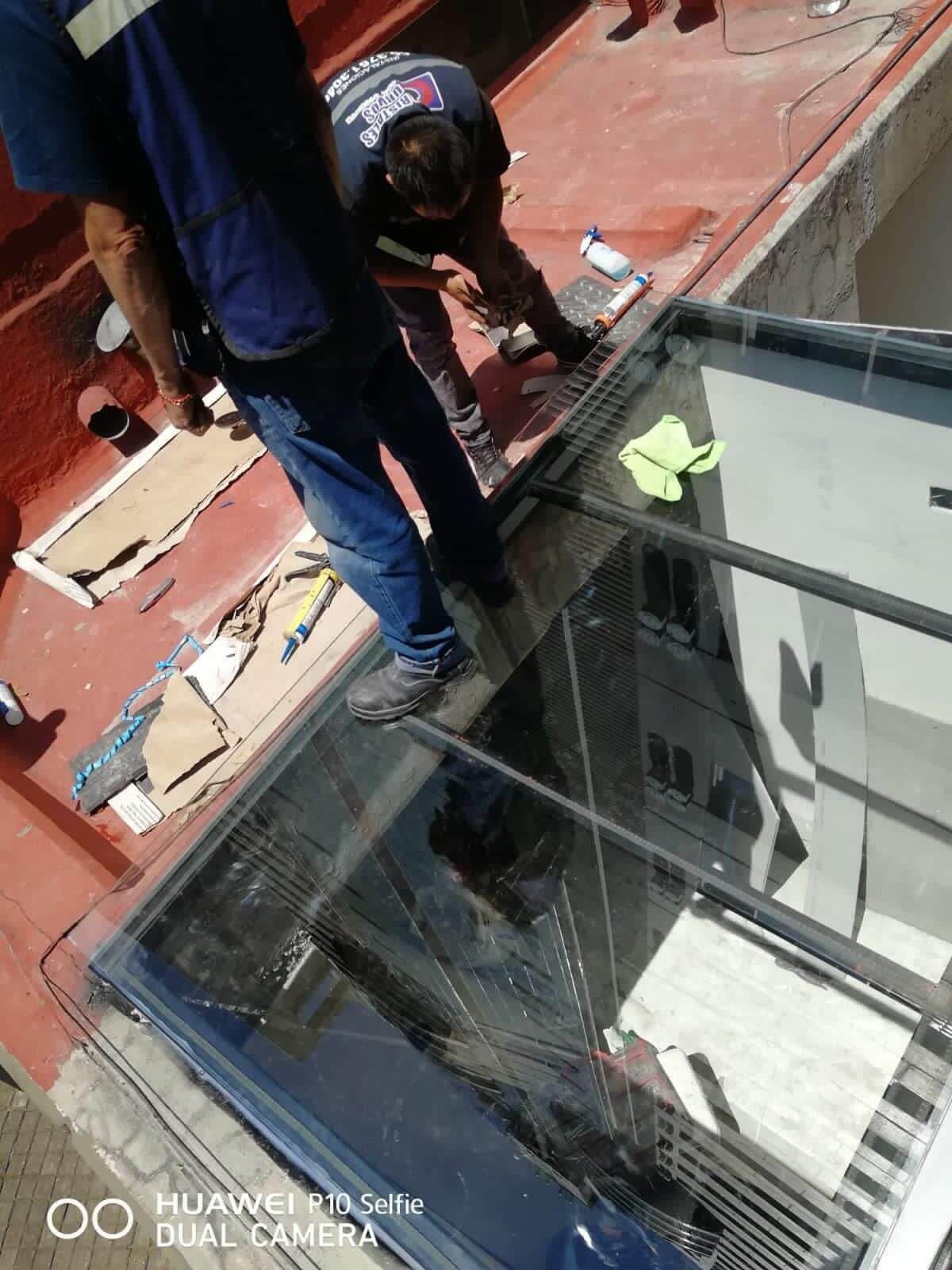 Un hombre está trabajando en una marquesina de vidrio en el techo de un edificio.