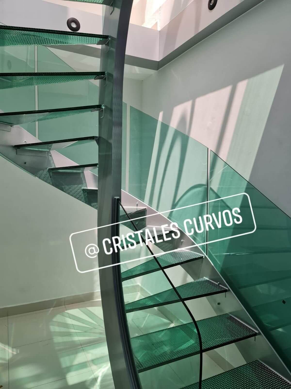 Una escalera de caracol con barandilla de cristal y un cartel que dice cristales curvos