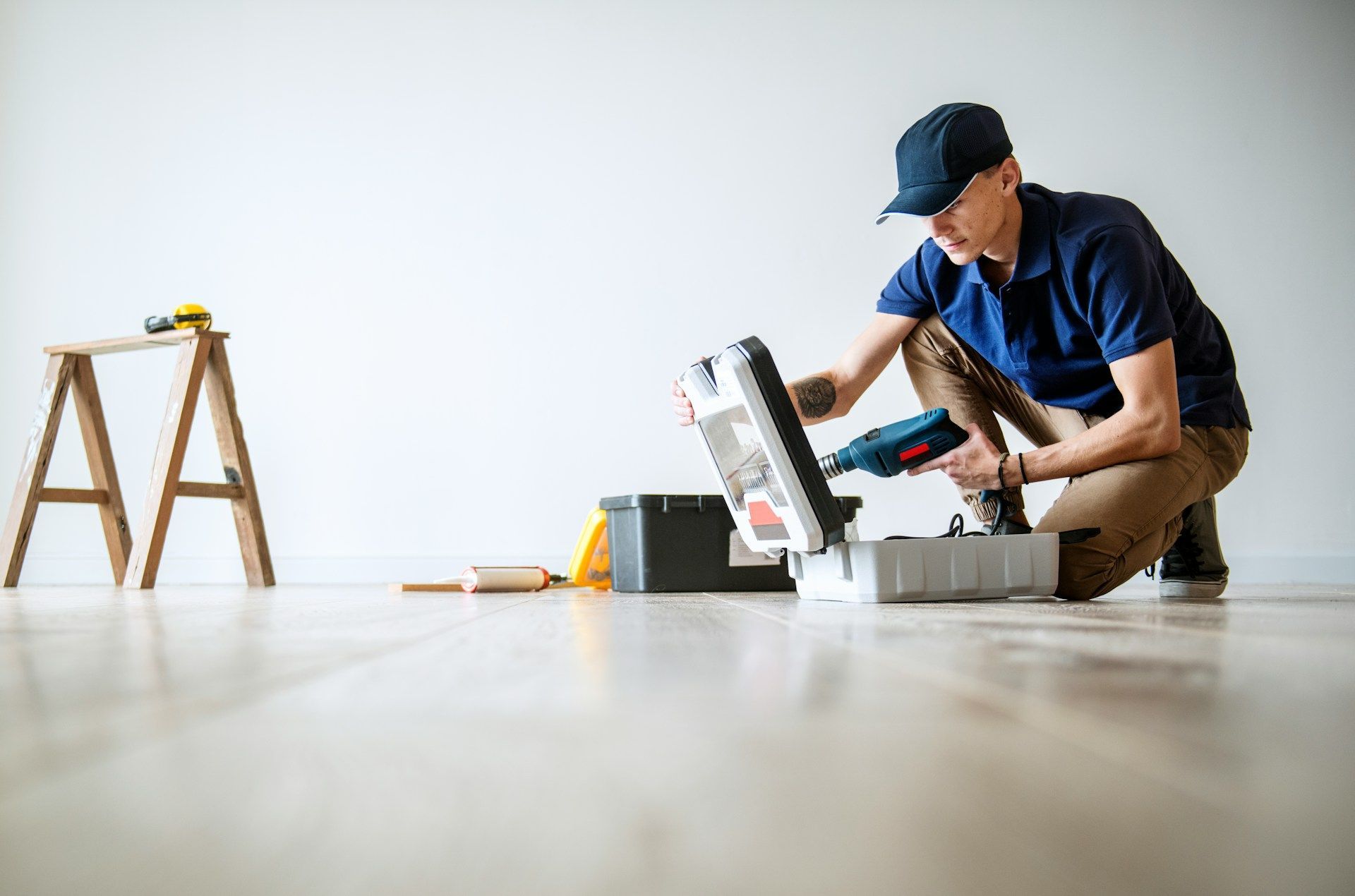 A person wearing a cap is using a saw. Tools and a toolbox are nearby.