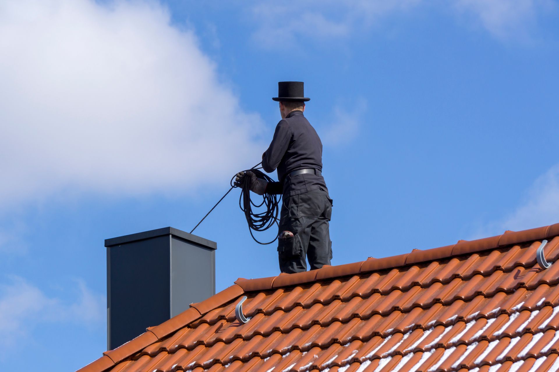 Chimney sweep on a rooftop, cleaning a chimney with a rope, blue sky in background.