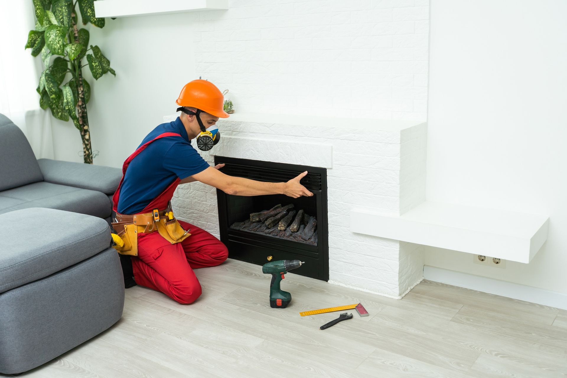 A worker in a respirator and hard hat installs a fireplace.