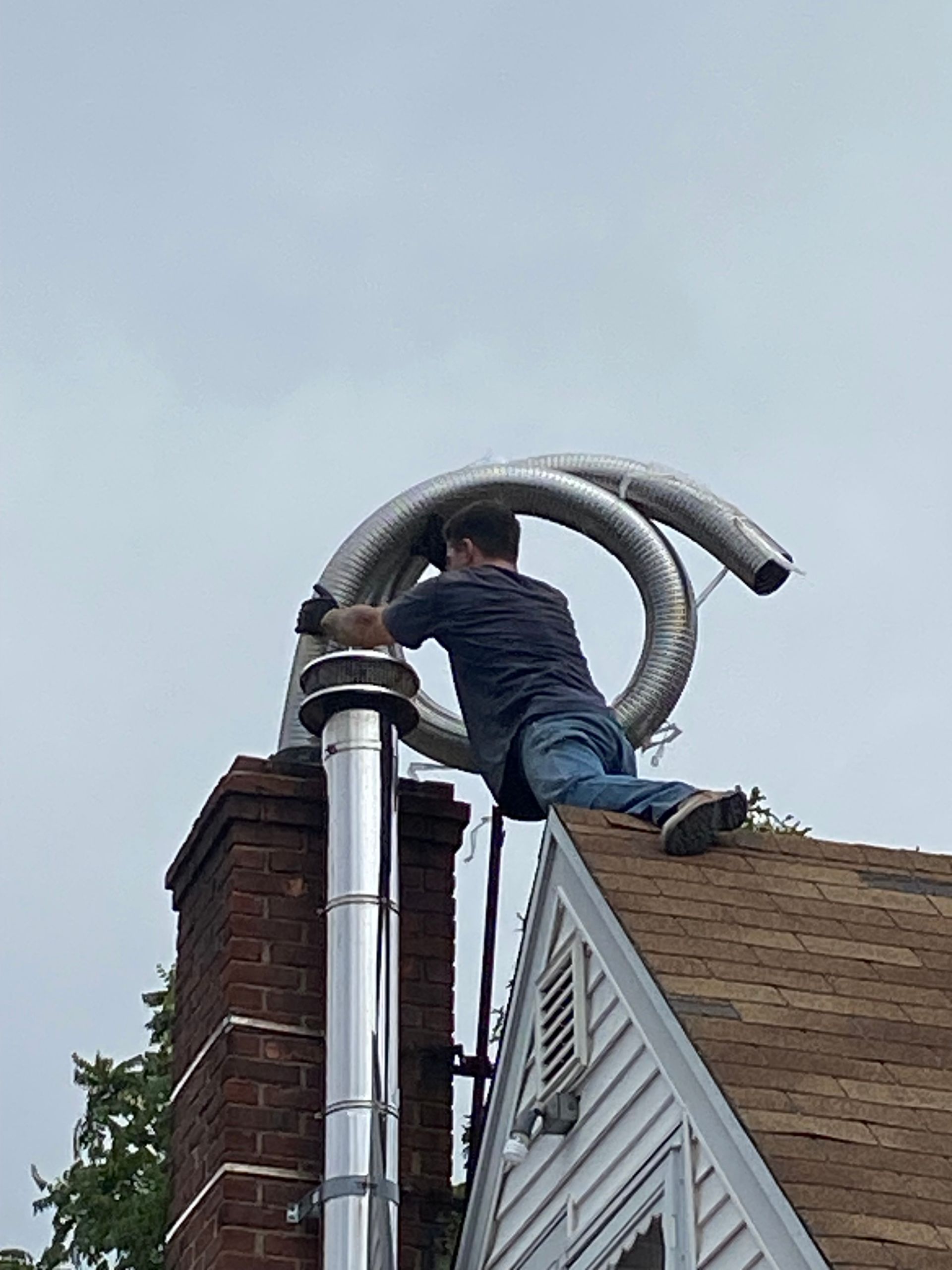 Person on a roof installing a flexible metal chimney liner. Grey sky overhead.