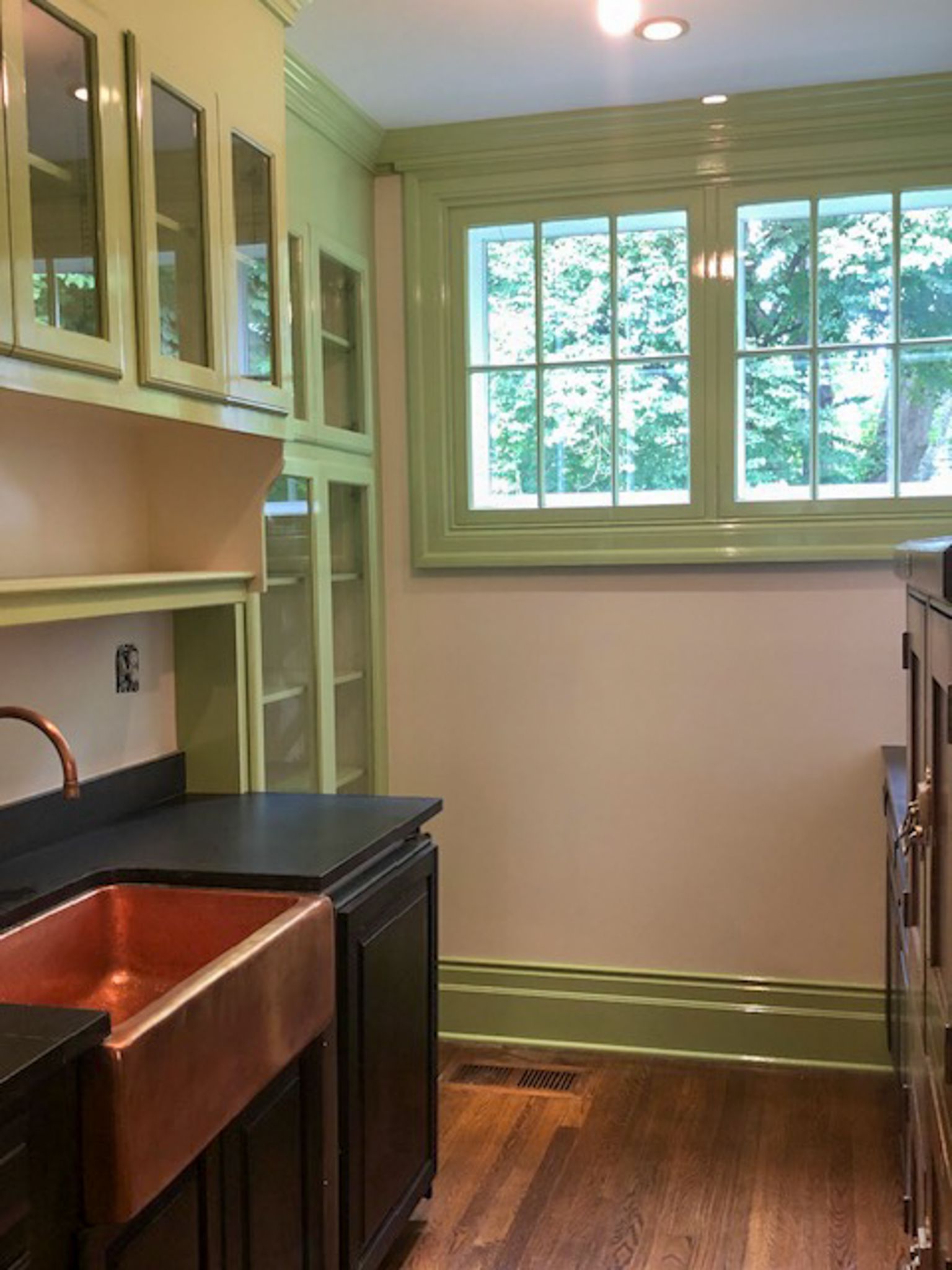 A kitchen with green cabinets and a copper sink