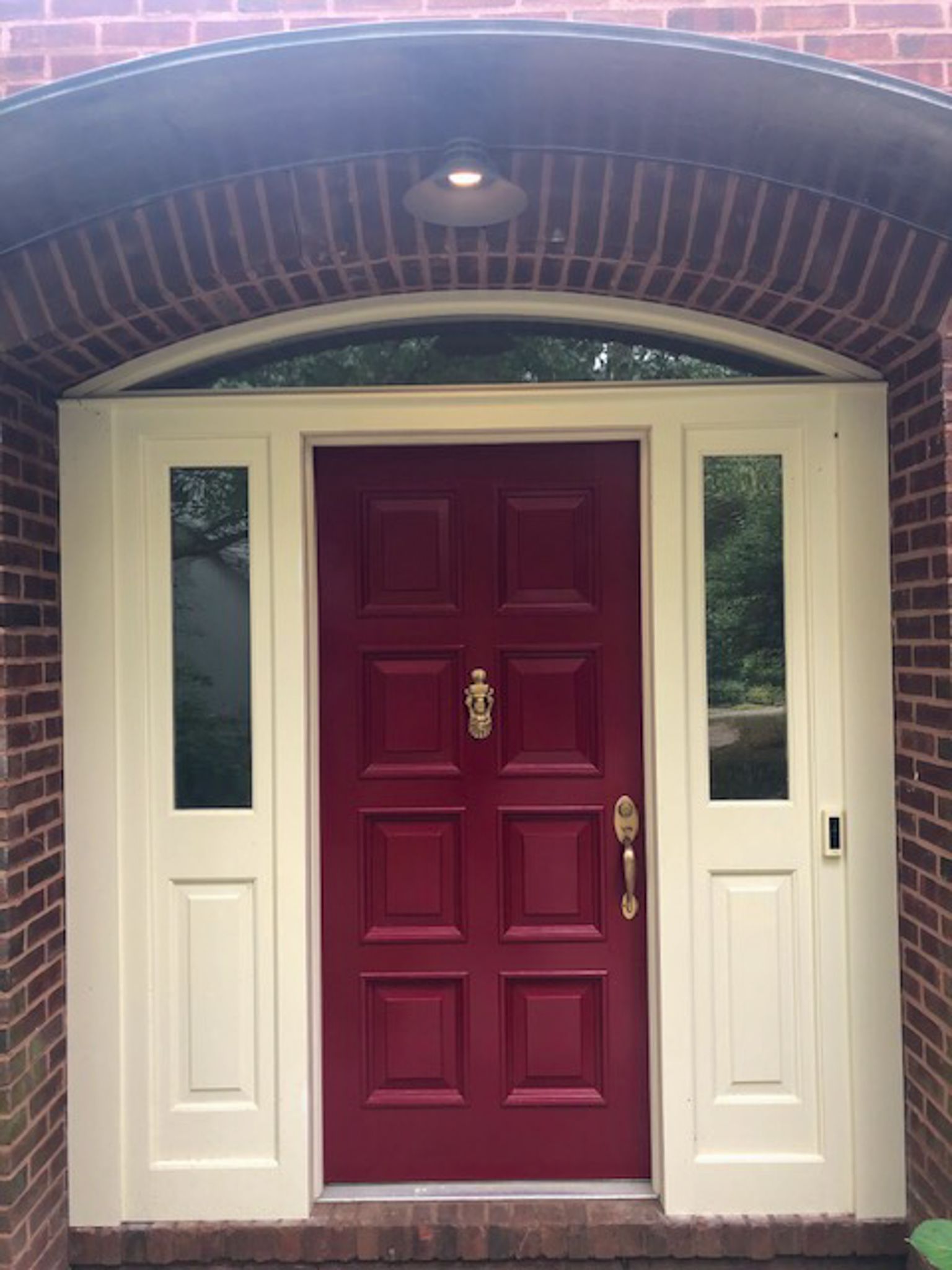 The front door of a brick house with a red door and white trim.