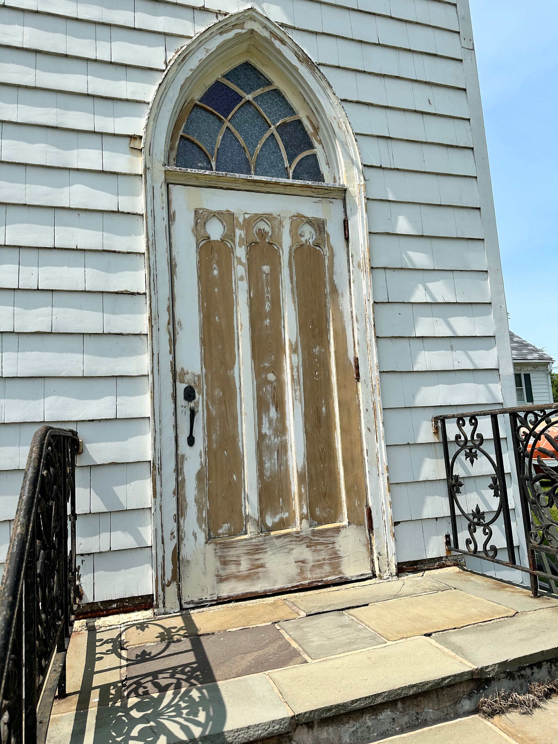 A white door with a stained glass window is on the side of a building.