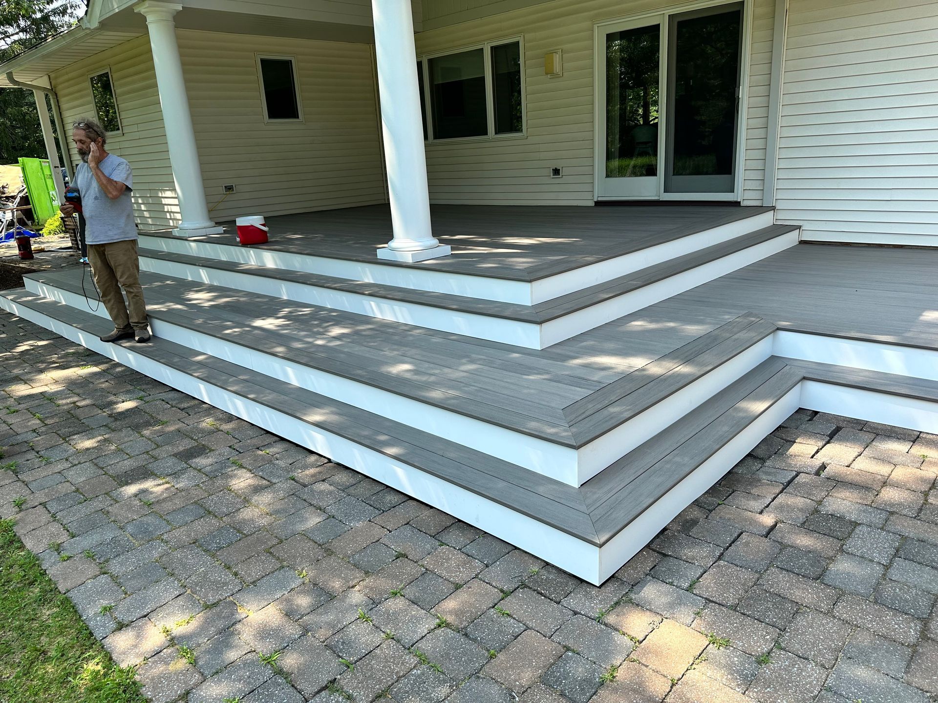 A man is standing on a deck next to a house talking on a cell phone.