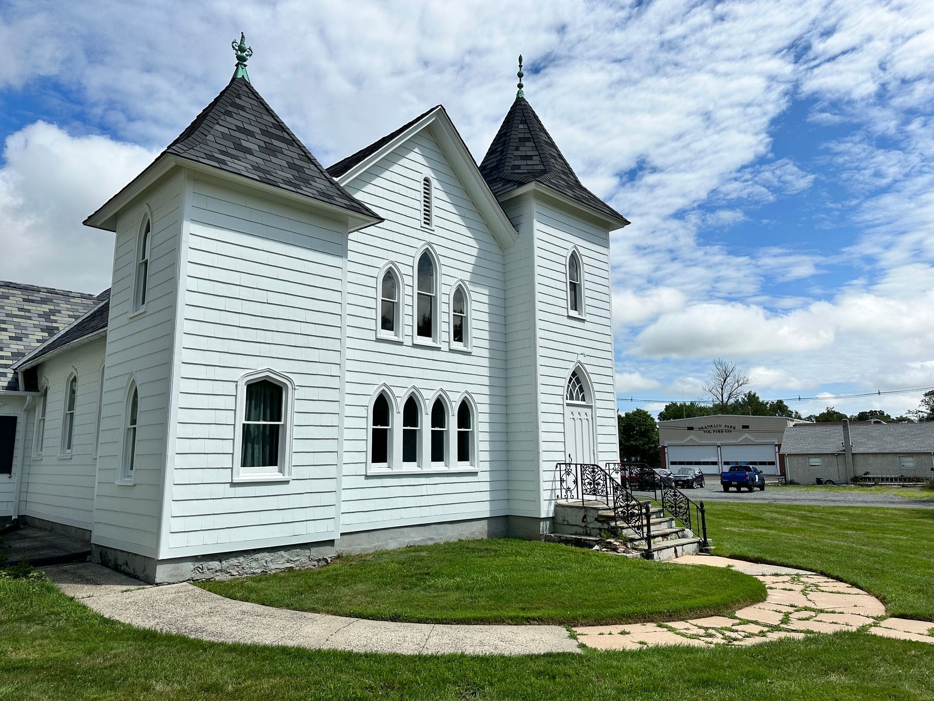 A large white house with a gray roof is sitting on top of a lush green field.