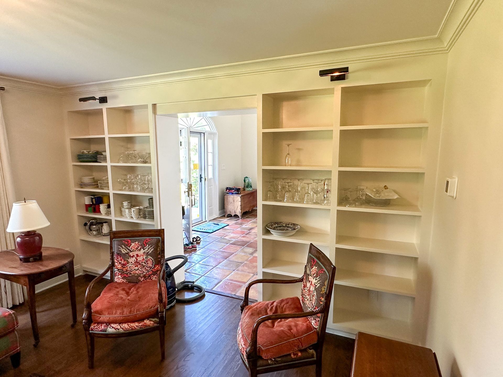 A living room with two chairs , a table , a lamp and shelves.