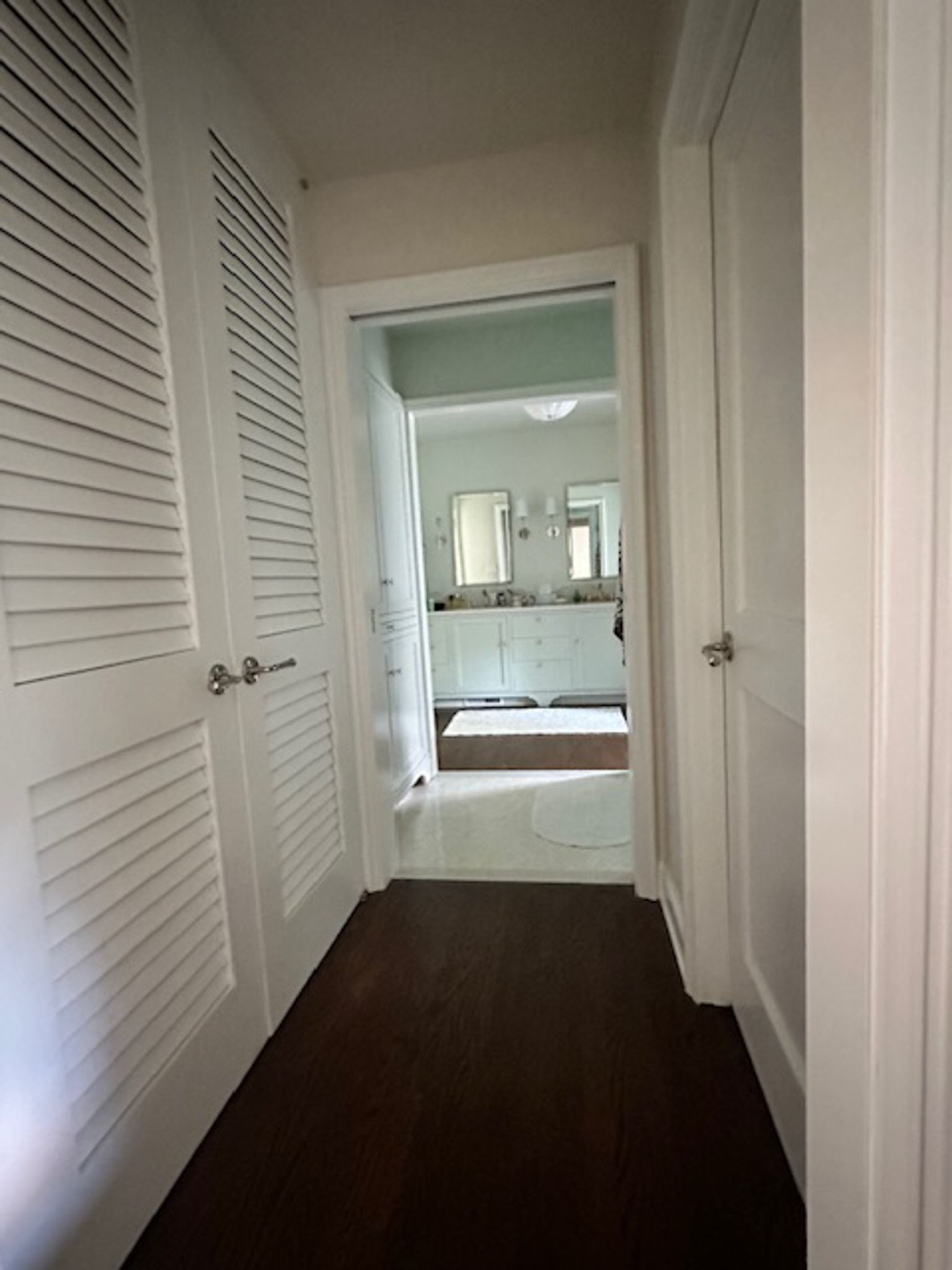 A hallway leading to a bathroom with two sinks and a bathtub.