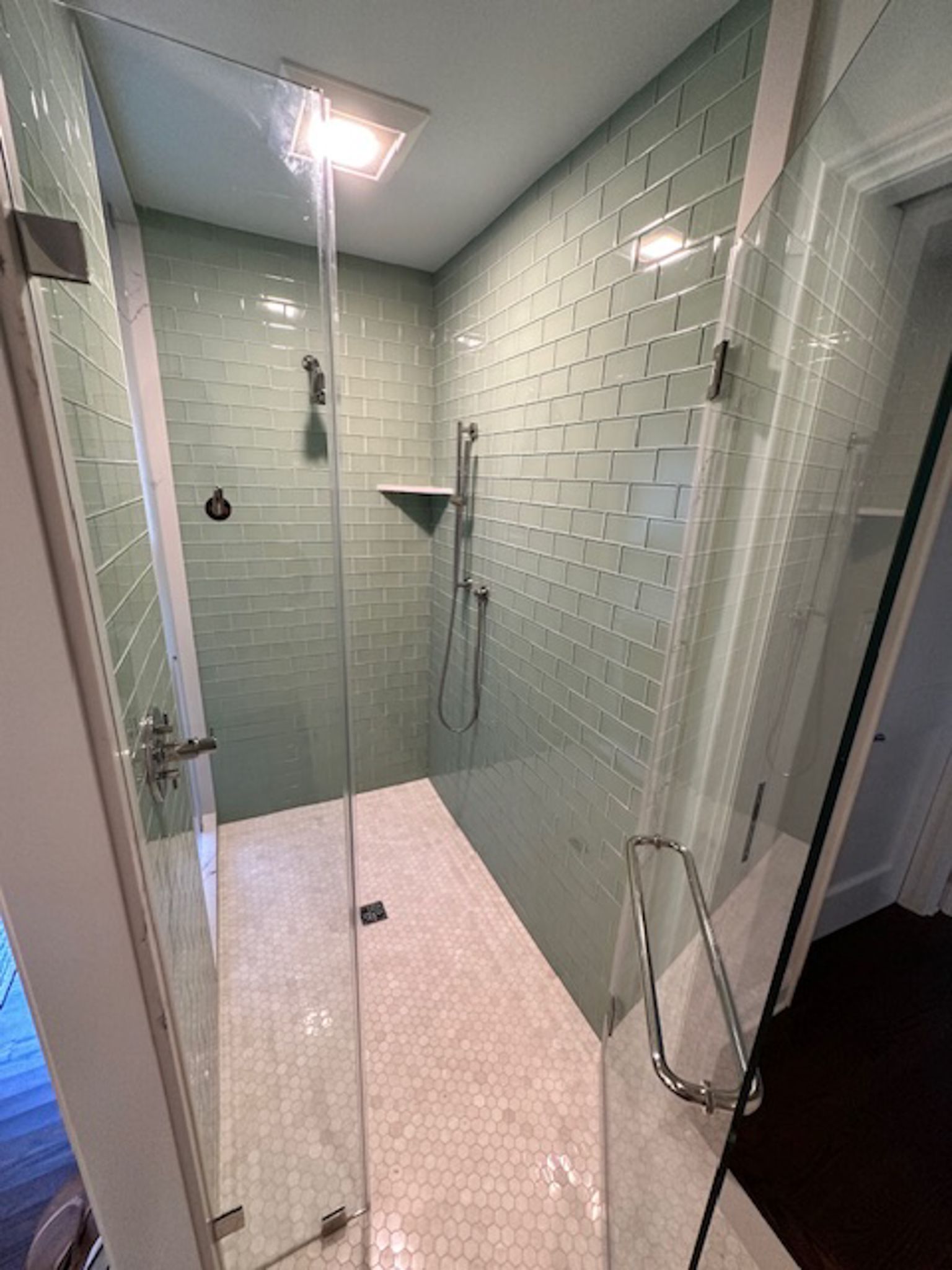 A bathroom with green tiles and a walk in shower with a glass door.