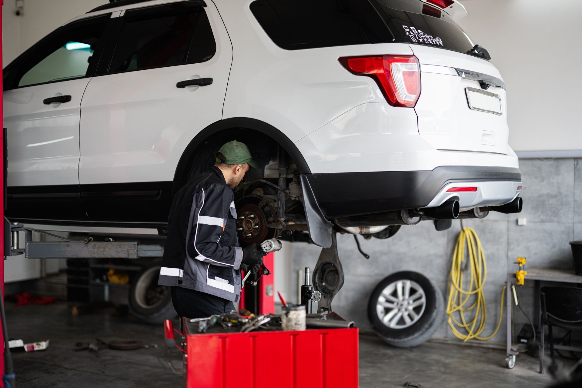 Mechanic working on a white SUV raised on a lift in a garage.