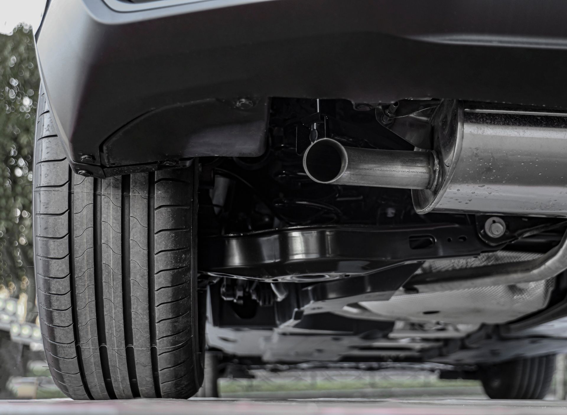 Undercarriage of a black car, showing the exhaust pipe, tire, and suspension components.