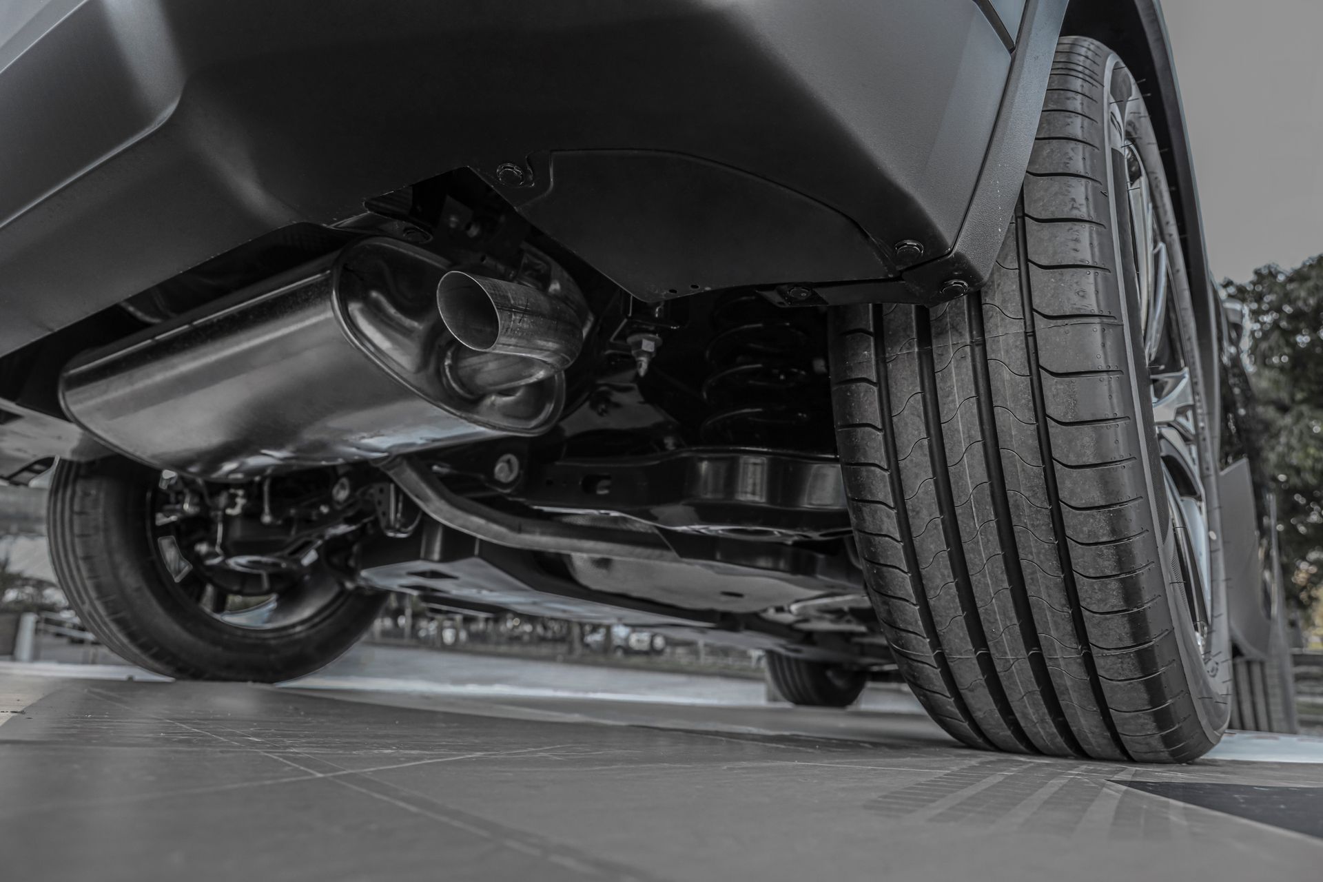 Undercarriage of a black car, showing exhaust pipe, tires, and suspension.