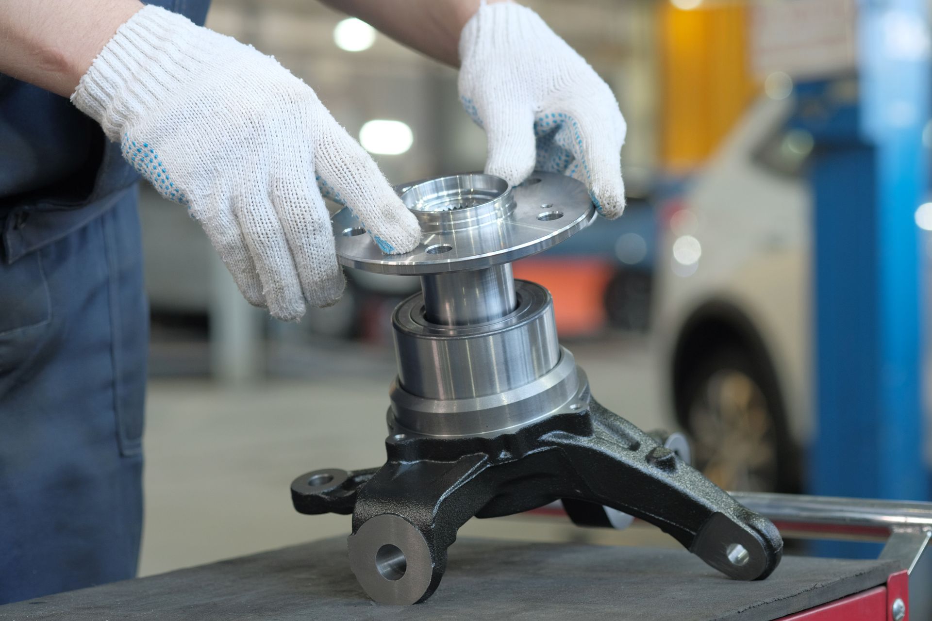 Mechanic's hands in white gloves assembling car part, including a hub, in a shop.