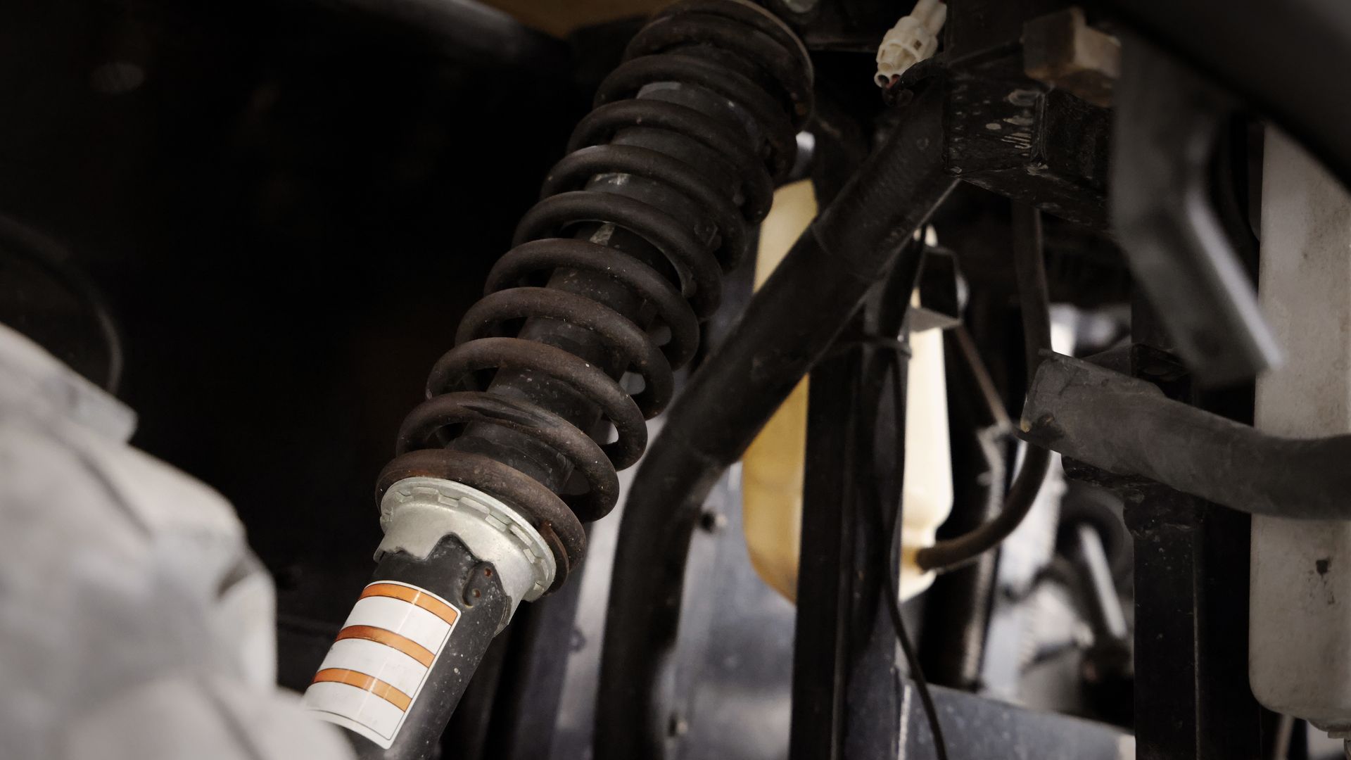 Close-up of a rusty coil spring shock absorber with wires and hoses, likely from a vehicle.