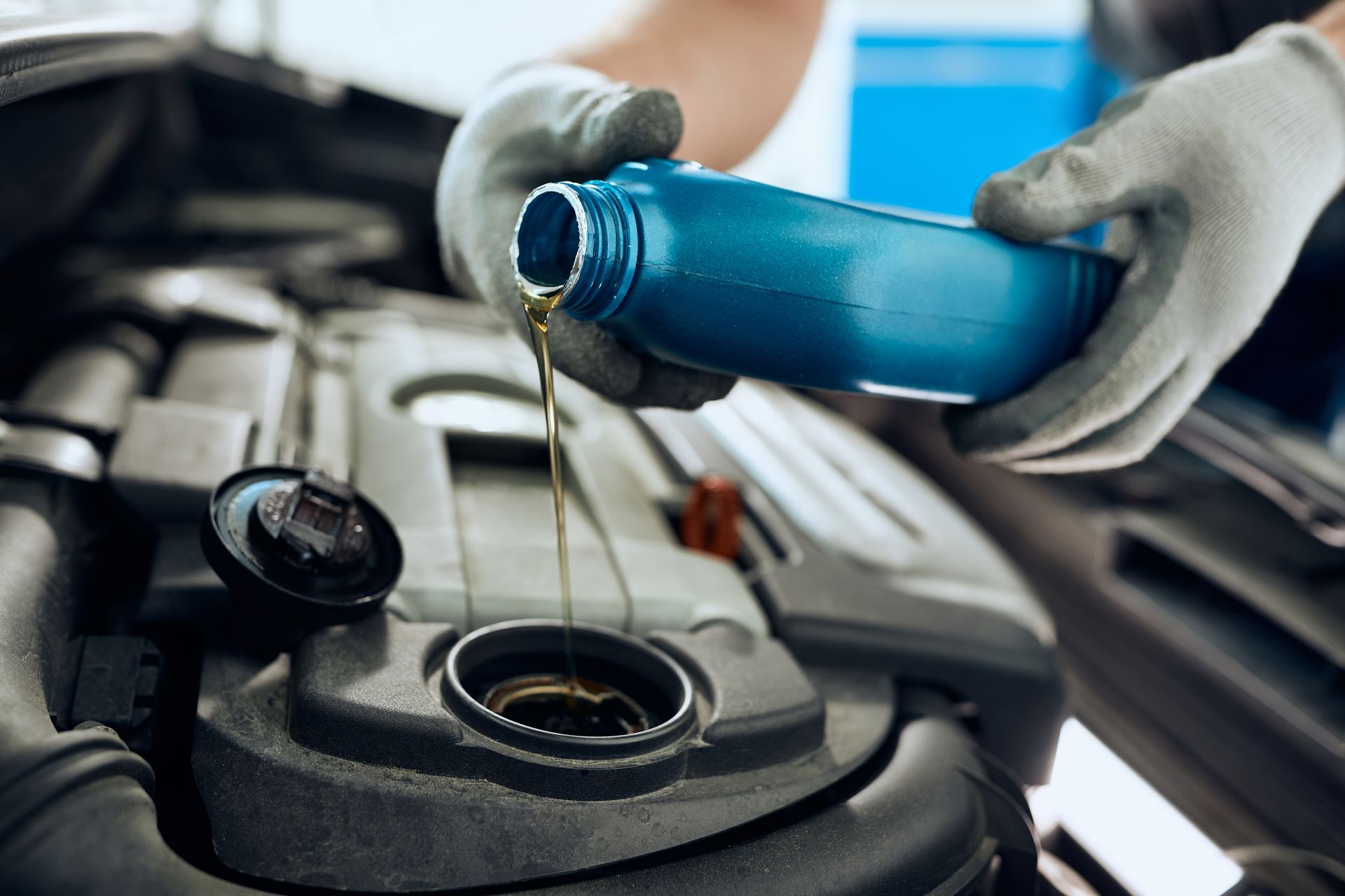 Gloved hand pouring oil from a blue bottle into a car engine, inside a vehicle.