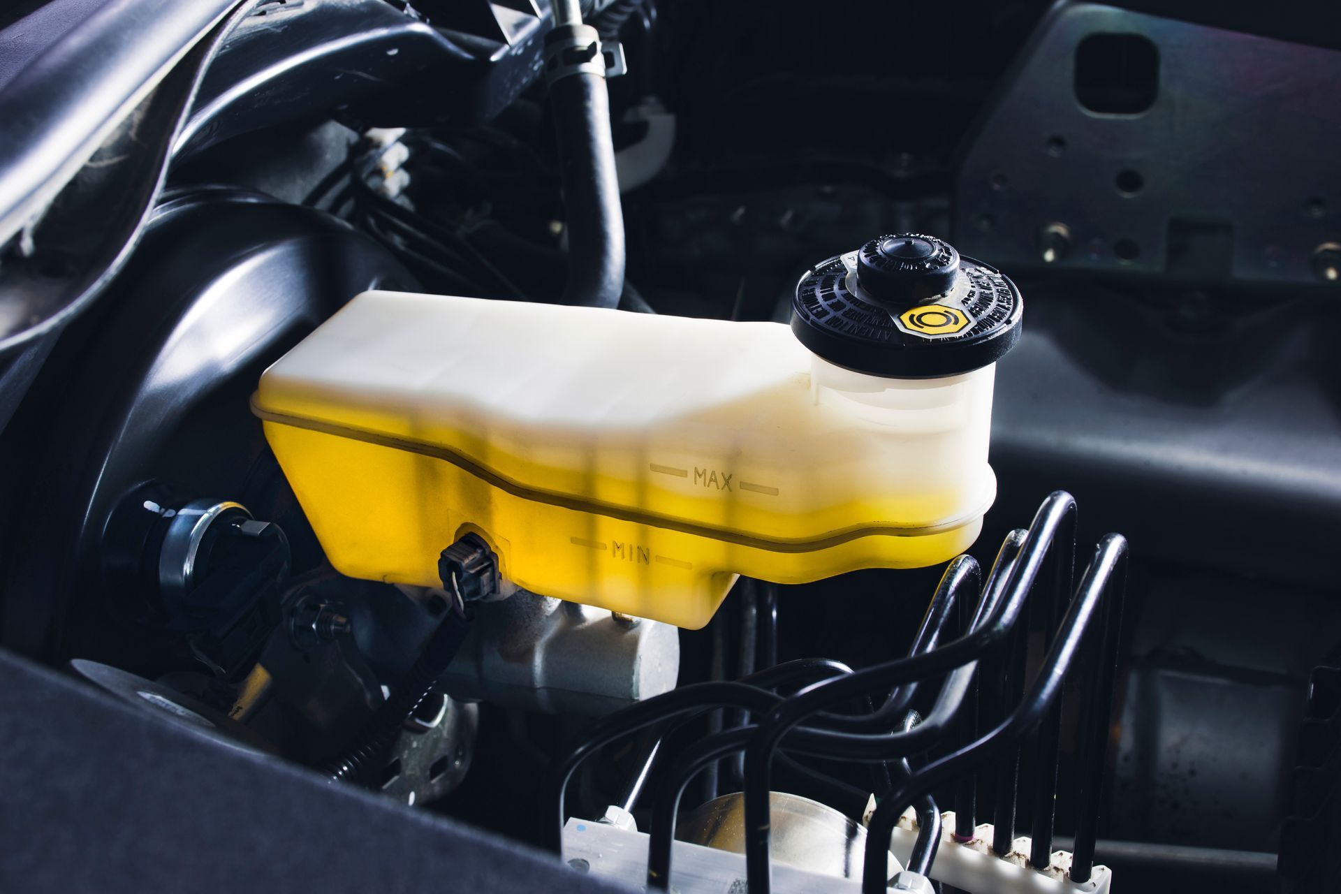 Brake fluid reservoir in a car engine compartment; yellow fluid, black cap.