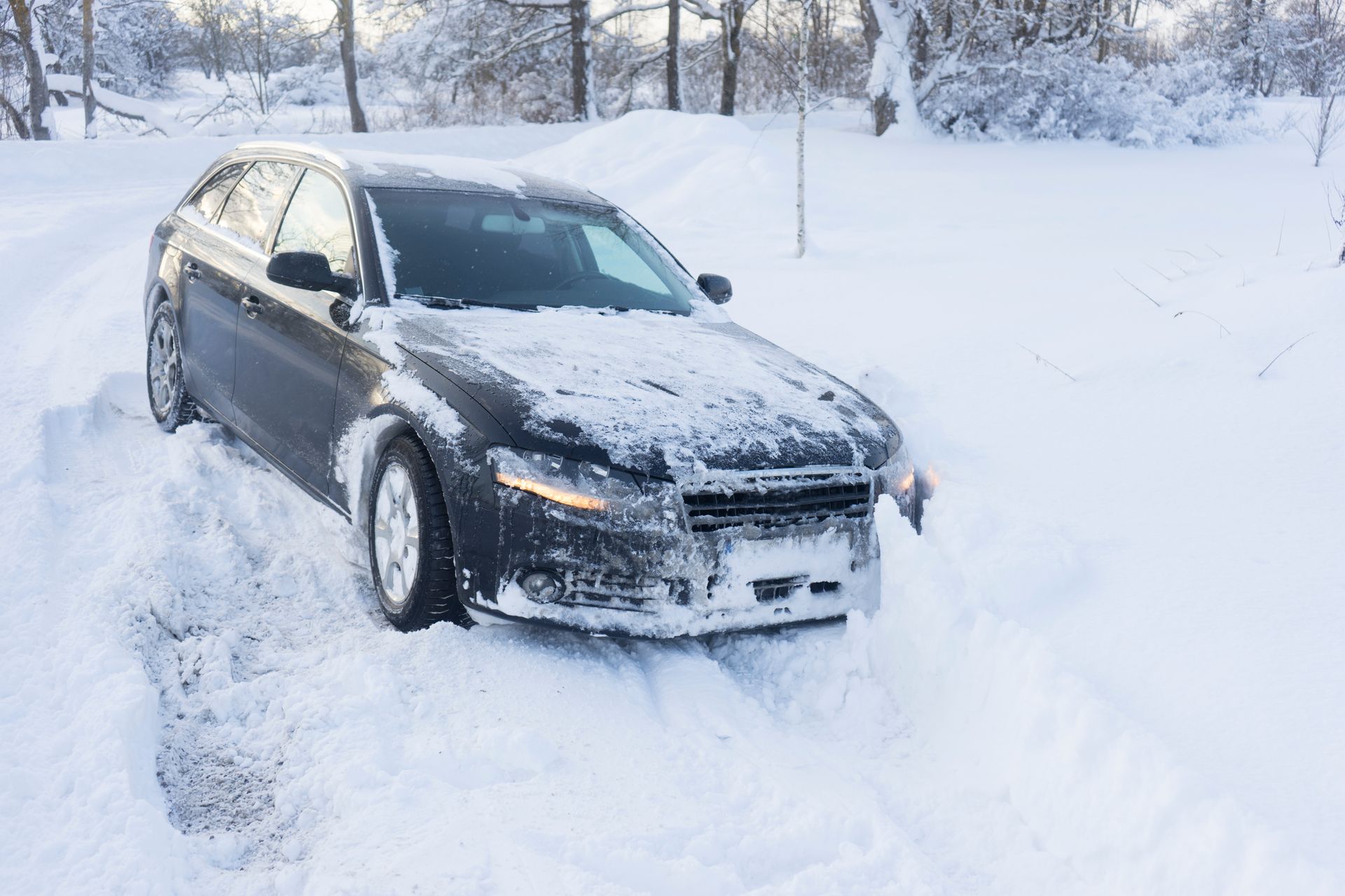 Dark car stuck in deep snow on a snow-covered road.