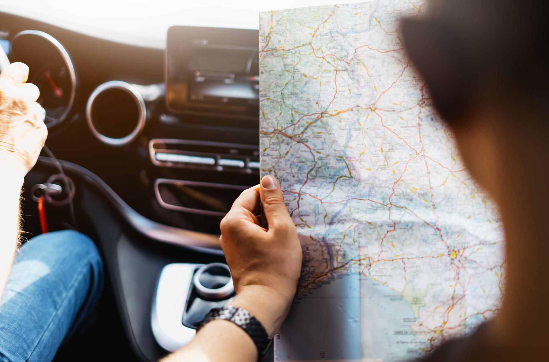 Passenger holding a paper map inside a car, with the dashboard and road visible.