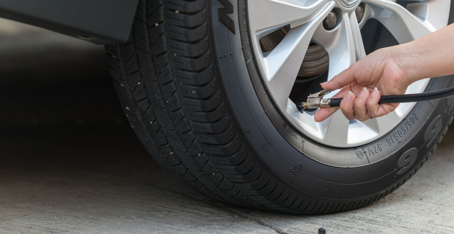 Person inflating a car tire with a black hose outdoors on concrete.