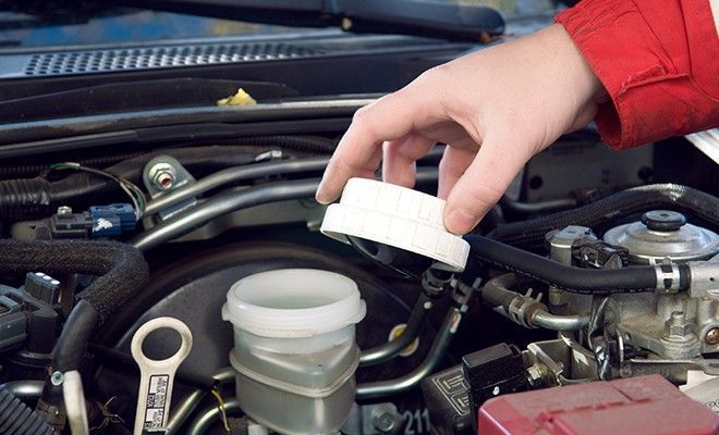 A person is pouring brake fluid into a container under the hood of a car
