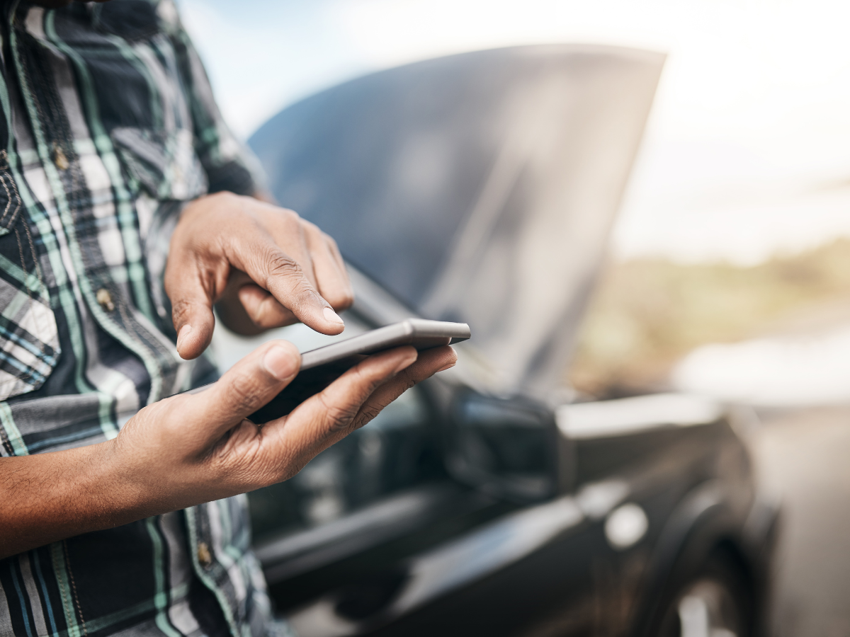 A man is using a cell phone in front of a broken down car. A man is using a cell phone in front of a broken down car.