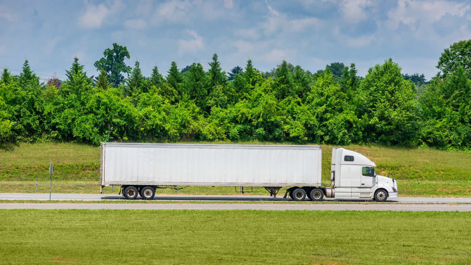 a white semi truck is driving down a highway next to a field .