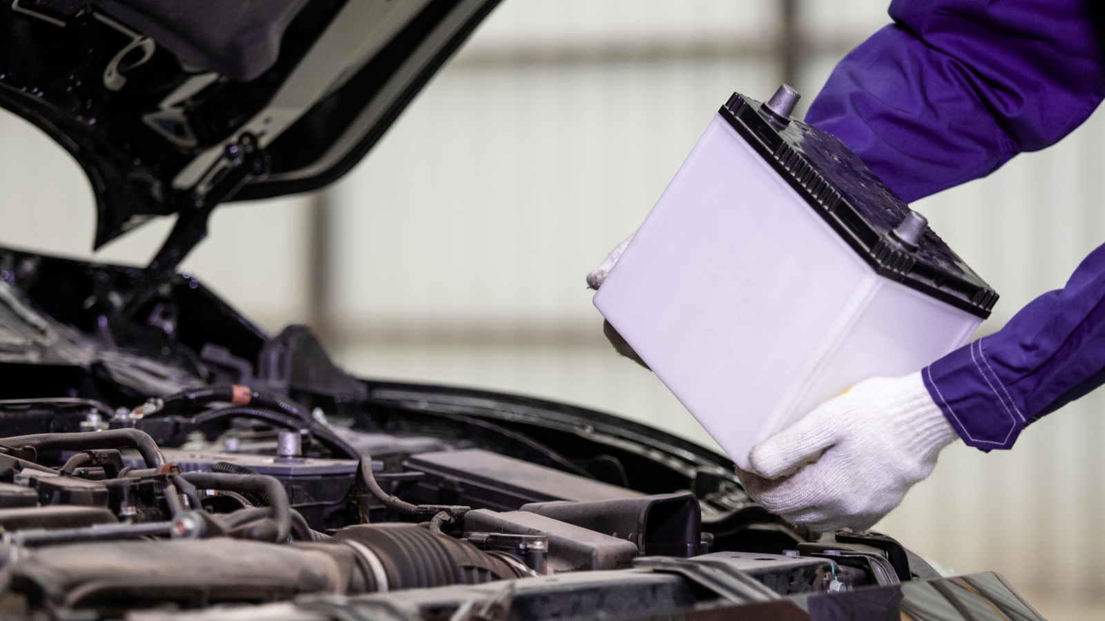 a person is holding a battery in front of a car with the hood open .