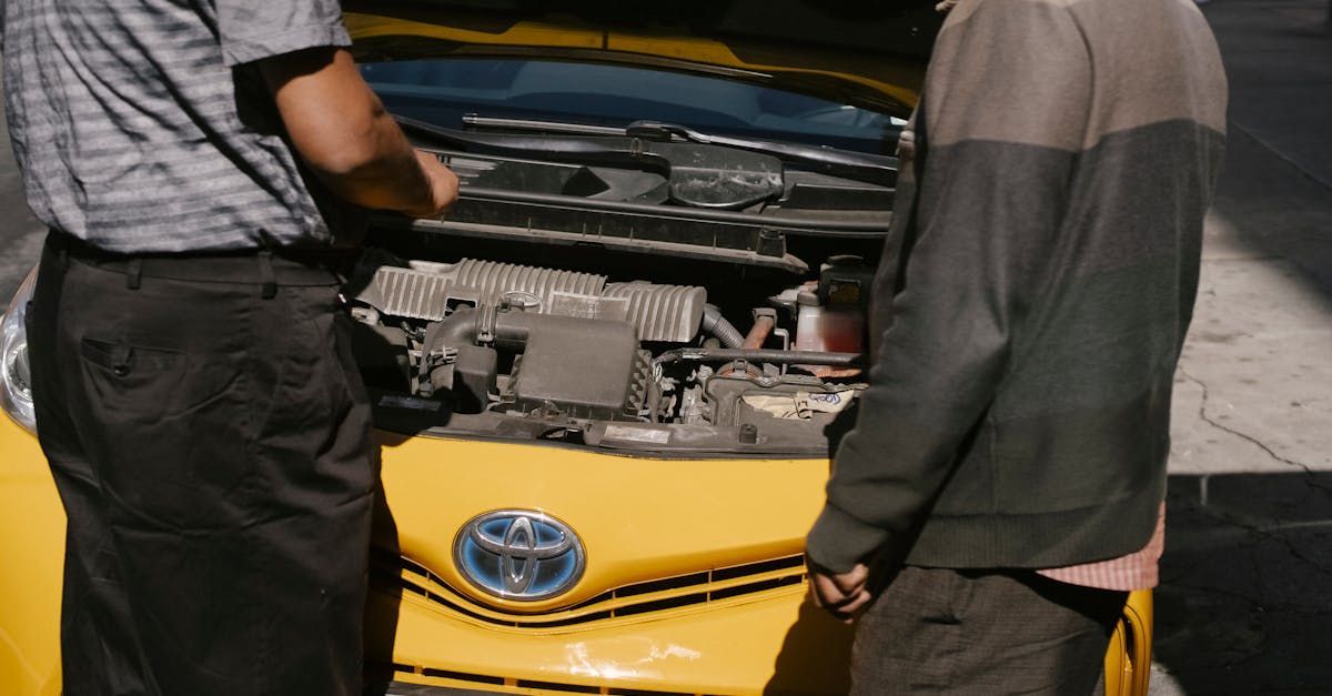 Two men are looking under the hood of a yellow car.