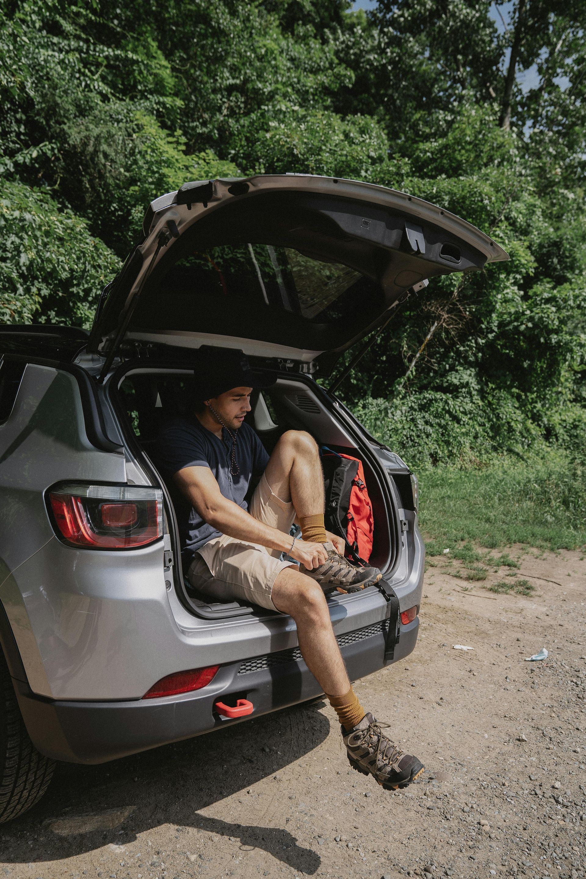 A man is sitting in the back of a car with the trunk open.