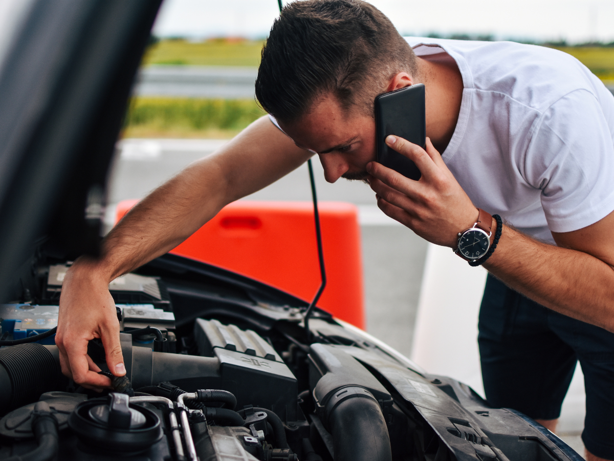 A man is talking on a cell phone while looking under the hood of a car. A man is talking on a cell phone while looking under the hood of a car.