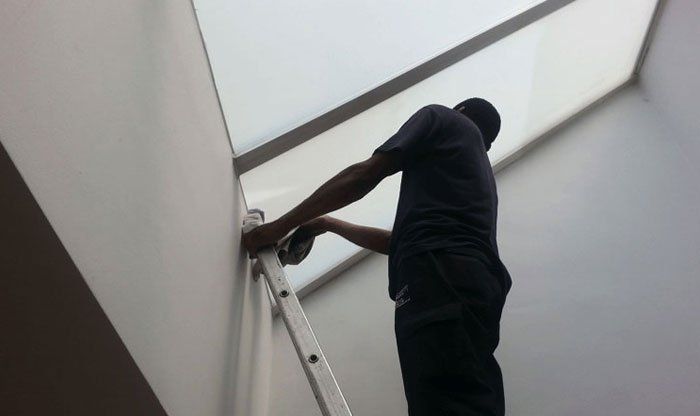 man up a ladder cleaning a window interior