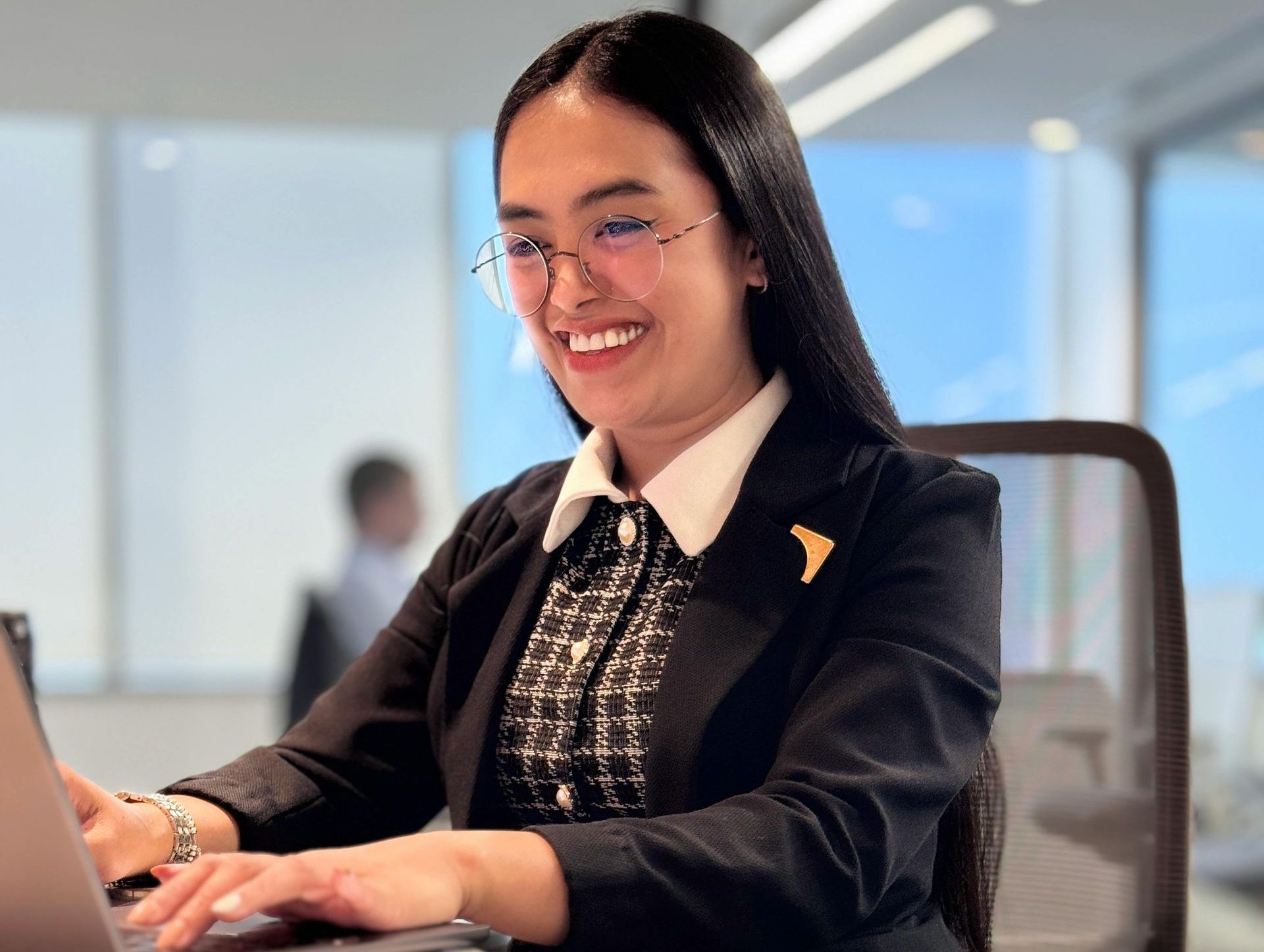 A woman is smiling while typing on a laptop computer.