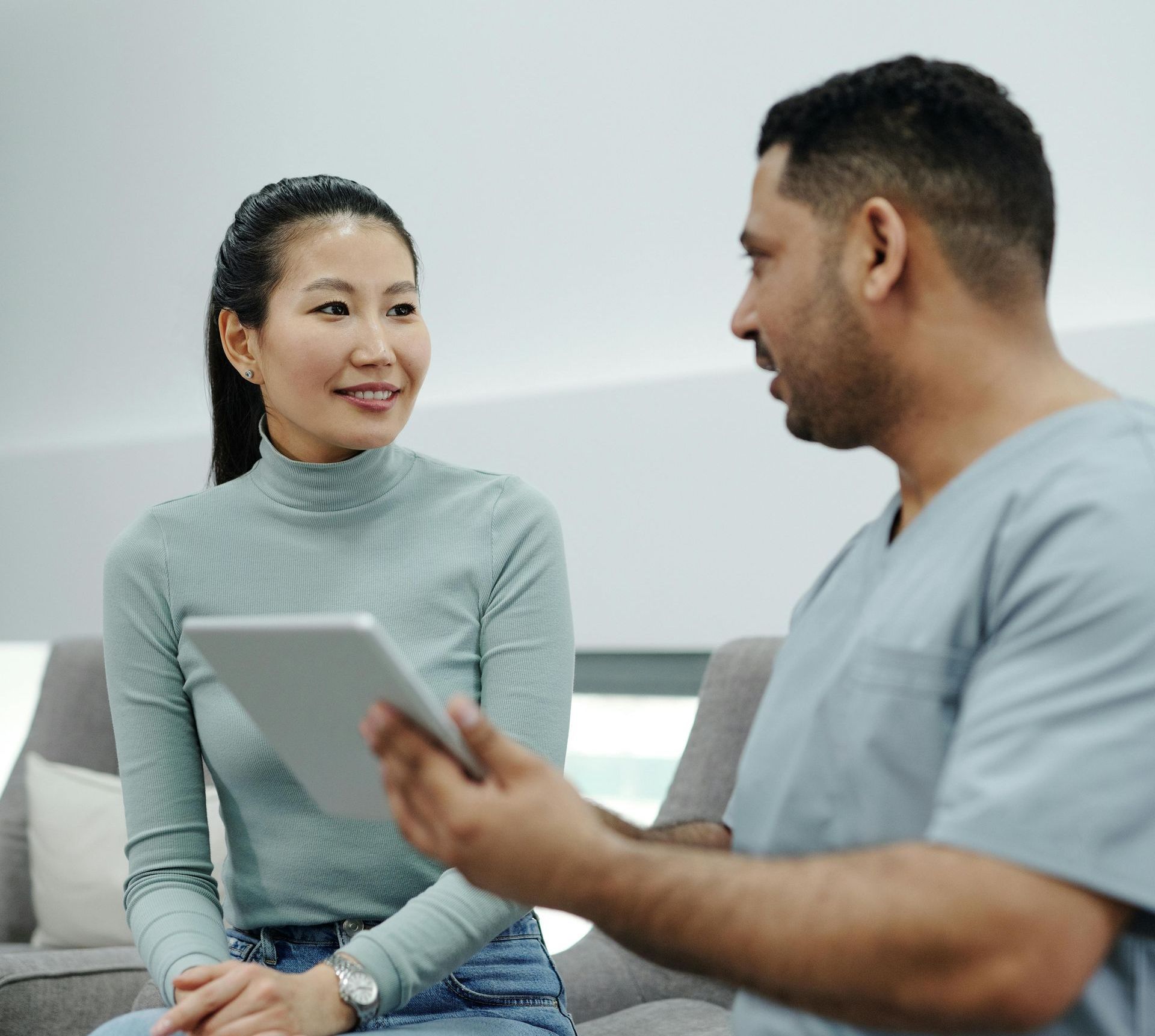 A man and a woman are sitting on a couch looking at a tablet.