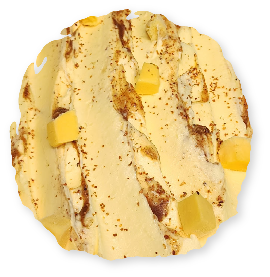 Top-down view of a swirl of yellow ice cream with dark brown streaks and yellow fruit chunks.