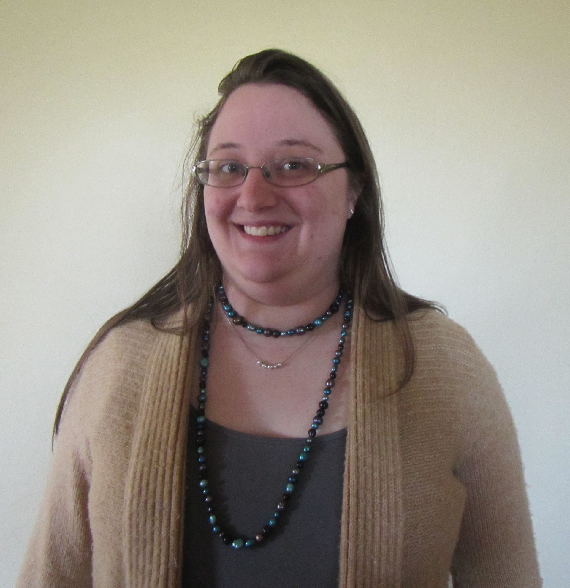 A woman wearing glasses and a necklace smiles for the camera