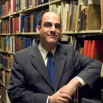 A man in a suit and tie is leaning against a bookshelf in a library