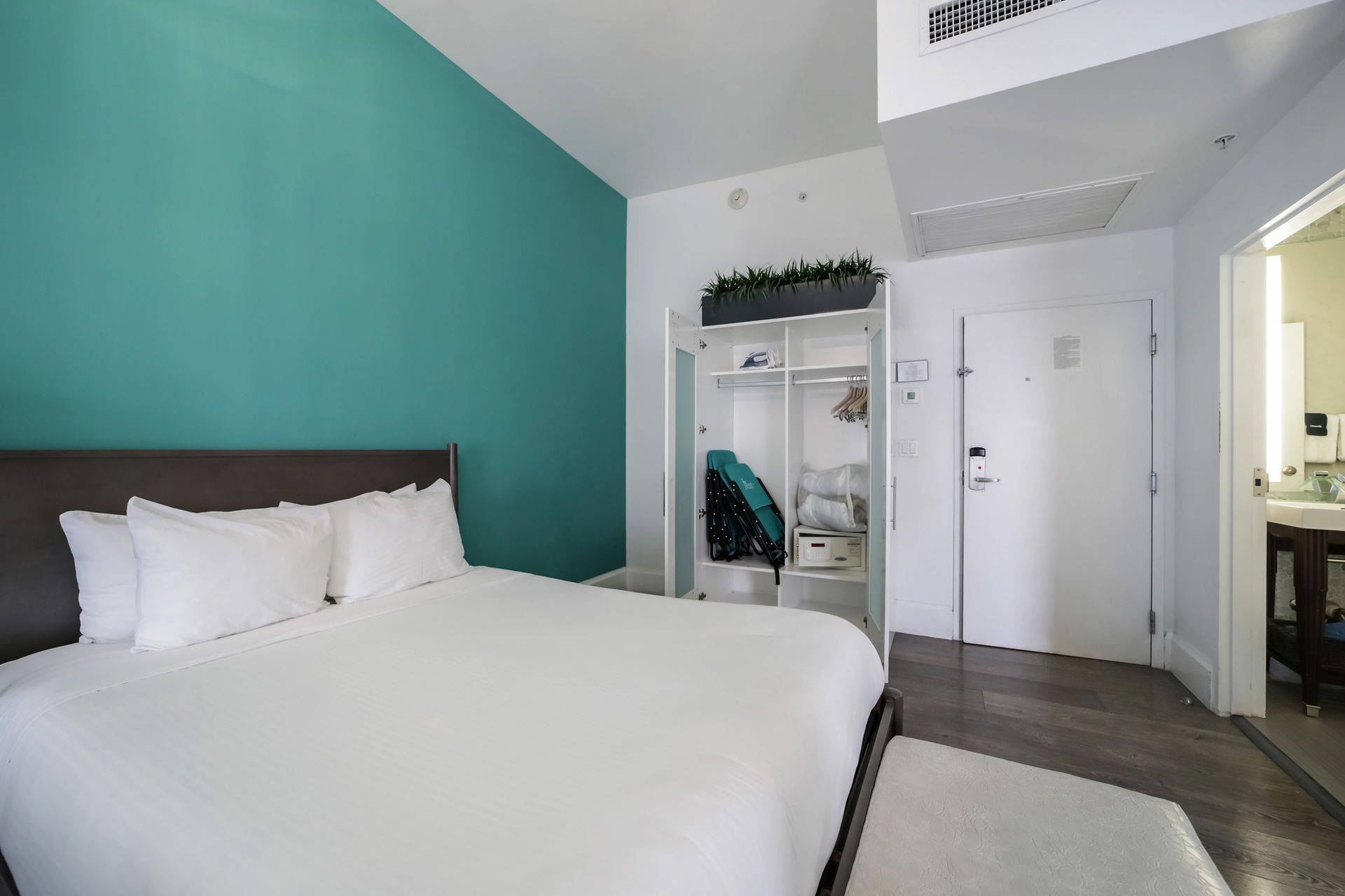 Bedroom with a teal accent wall, bed with white bedding, open closet, and doorway to a bathroom.