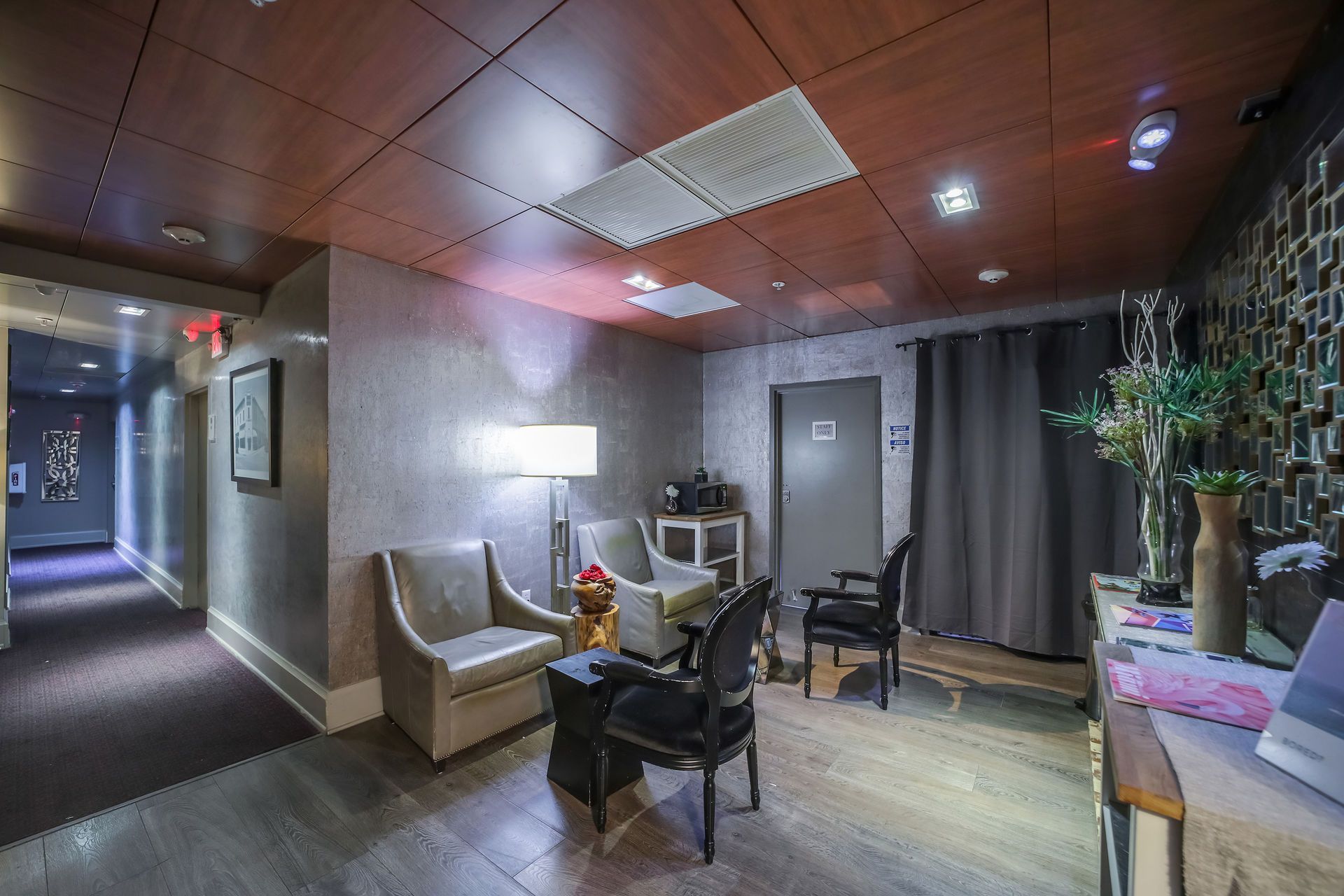 Lobby with seating, hallway to left, patterned accent wall, dark curtains, wooden ceiling.