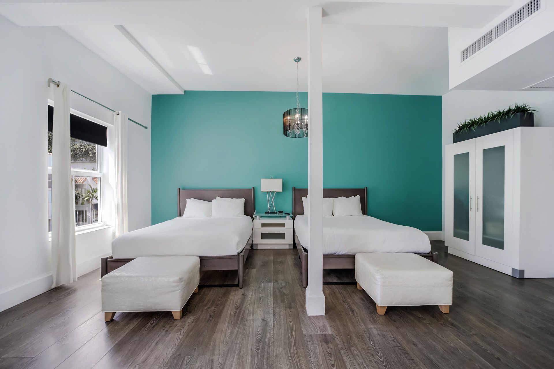 Two beds in a teal-walled hotel room, separated by a white pillar, with wood floors.