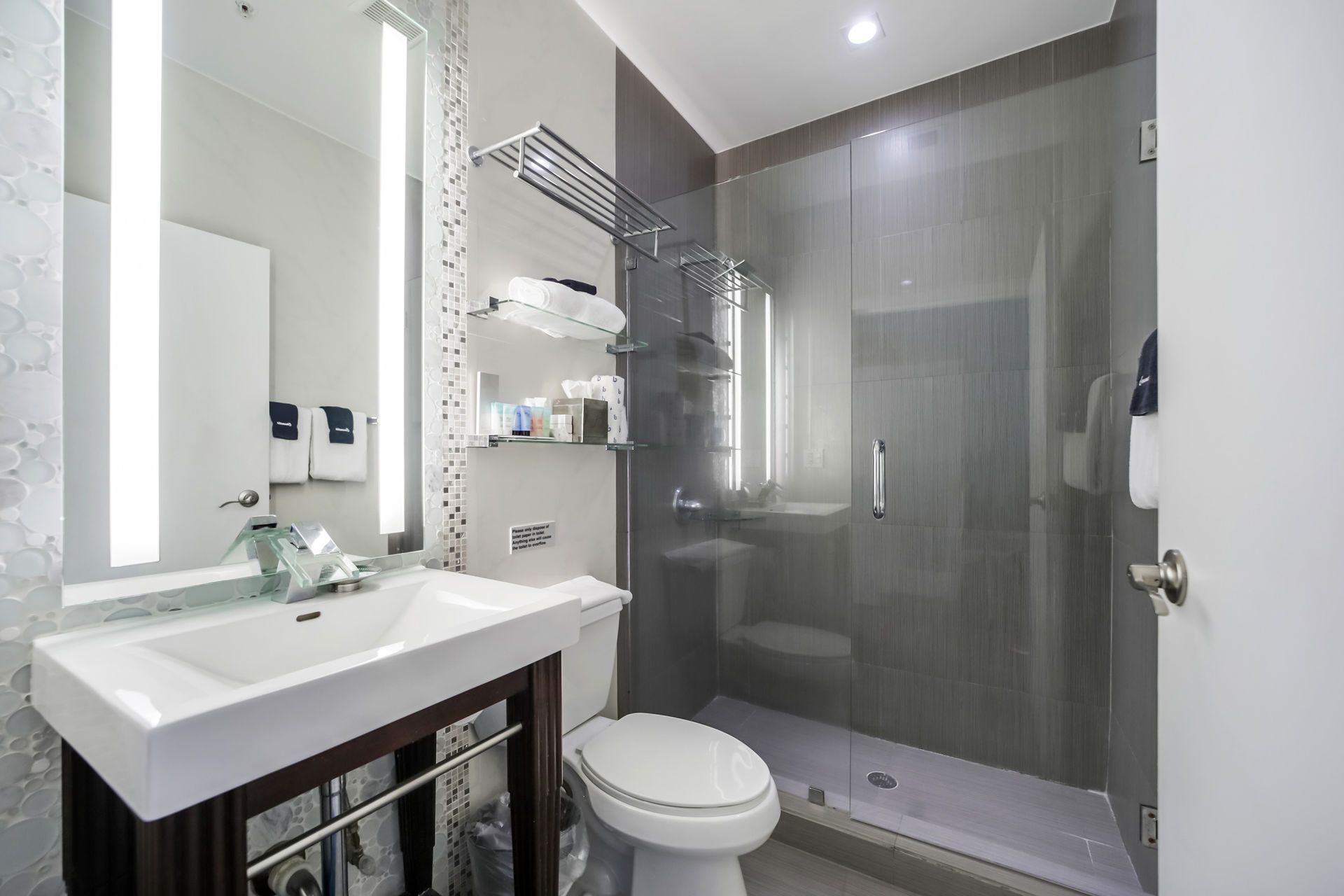 Modern bathroom with a glass shower, toilet, sink, and mirror. White and gray tones.